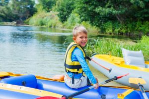 Active happy child having fun adventurous experience kayaking on the river on a sunny day during summer vacation