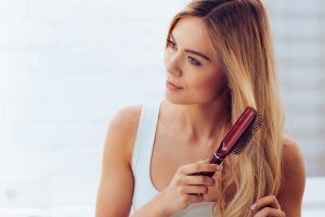 Close-up of beautiful young woman brushing her long hair and looking away while standing against white brick wall