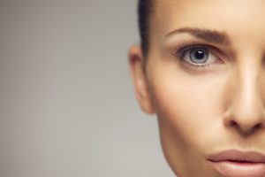 Close-up portrait of pretty young woman with perfect healthy skin and beautiful eyes. Half face of pretty young female against gray background