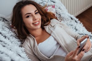 Portrait of a cheerful happy woman lying on sofa and holding mobile phone